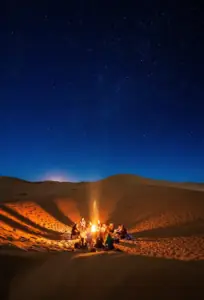 Campfire glowing on the dunes under a starry night sky in Morocco's Sahara Desert